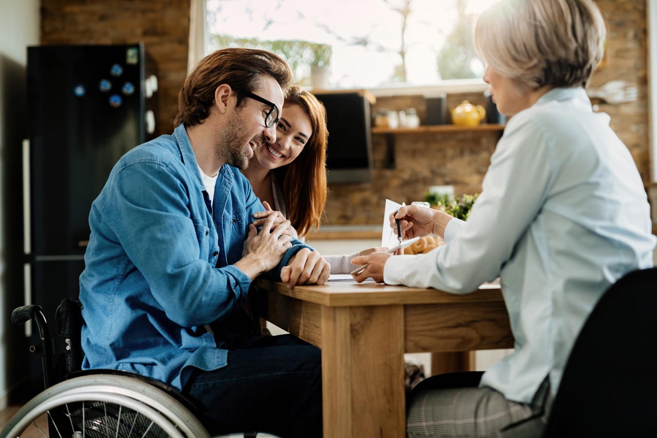 A financial advisor discussing Social Security disability benefits with a smiling couple, including a man in a wheelchair.