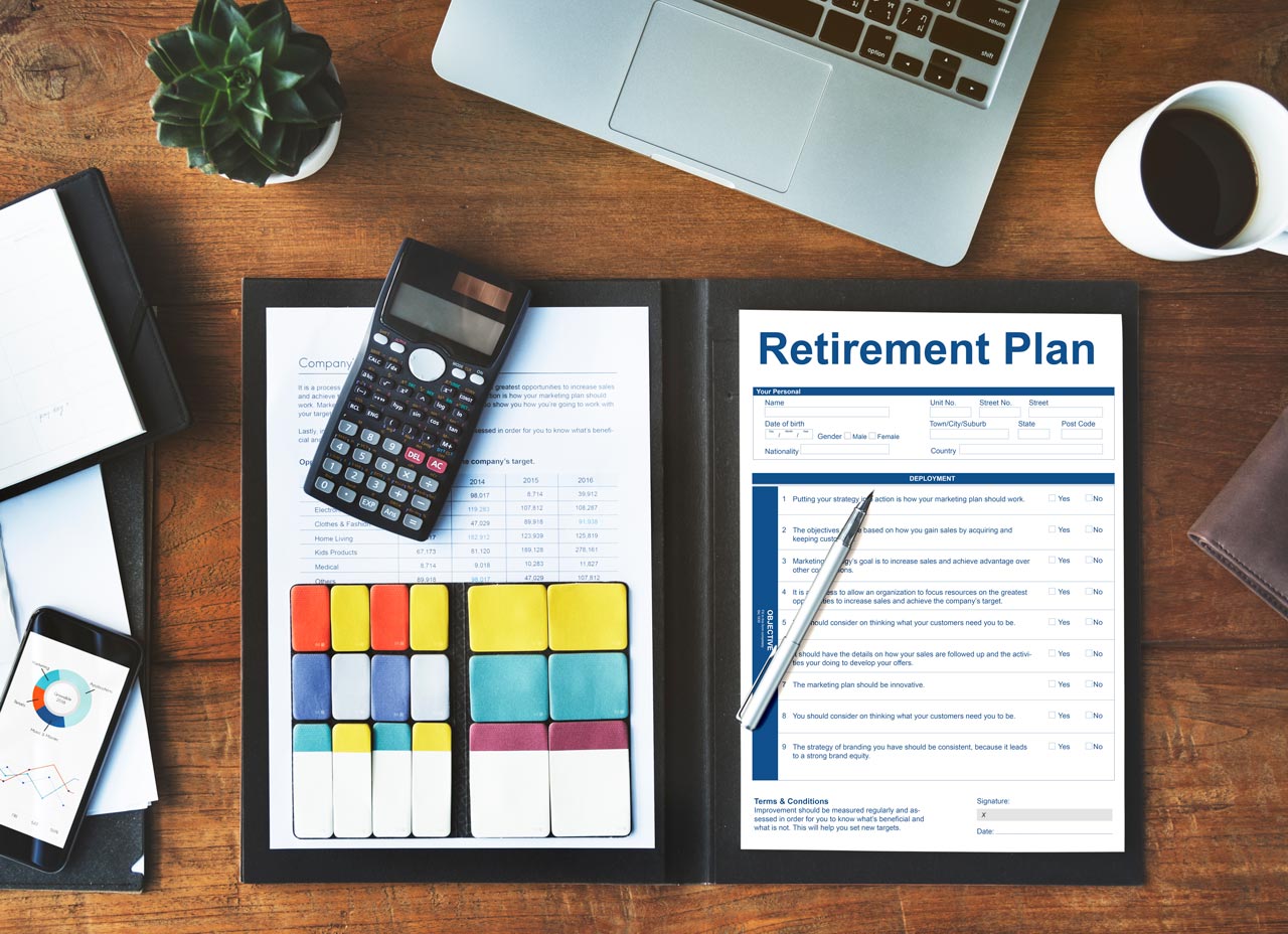 Retirement plan document on a desk with a calculator, pen, laptop, and financial charts. Financial planning for retirement income.